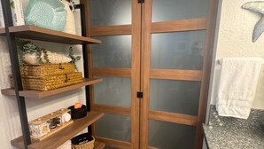 A wooden wardrobe with frosted glass doors, shelves with baskets, and a plant. - Oceanfront, swim with turtles, enjoy sunset views, all from your backyard. #B18 (Lahaina)