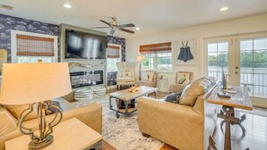 A living room with a fireplace, a ceiling fan, and a large window with a view. - Homosassa Riverfront Stay with Private Dock (Homosassa)