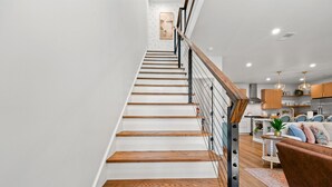 A staircase with wooden steps and a metal railing, leading to a living area with a sofa and a coffee table. - Hidden Haven | 5 mins to Folly, Luxury New Build (Charleston)