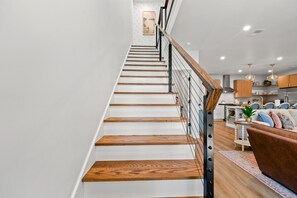 A staircase with wooden steps and a metal railing, leading to a living area with a sofa and a coffee table. - Hidden Haven | 5 mins to Folly, Luxury New Build (Charleston)
