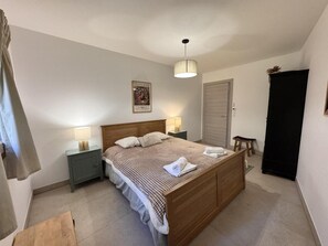 Ein Schlafzimmer mit einem hölzernen Bett, zwei Nachttischen mit Lampen, einer Tür und einem kleinen Hocker.