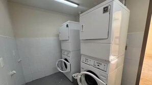 Una lavanderia con lavatrici e asciugatrici affiancate, pareti piastrellate bianche e un lampadario al neon.
