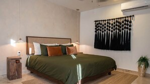 Una camera da letto ordinata con un letto, comodini, un condizionatore d'aria a parete e un arazzo appeso.