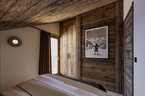 Ein Zimmer mit Holzbalkendecke, einem gerahmten Bild eines Skifahrers und einem Bett mit weißer Matratze.