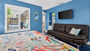 Un dormitorio con cama, un sofá de cuero marrón, televisión y ventana con persianas.
