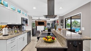Cocina moderna con encimeras de granito, una isla central con fruta y vistas a una piscina.