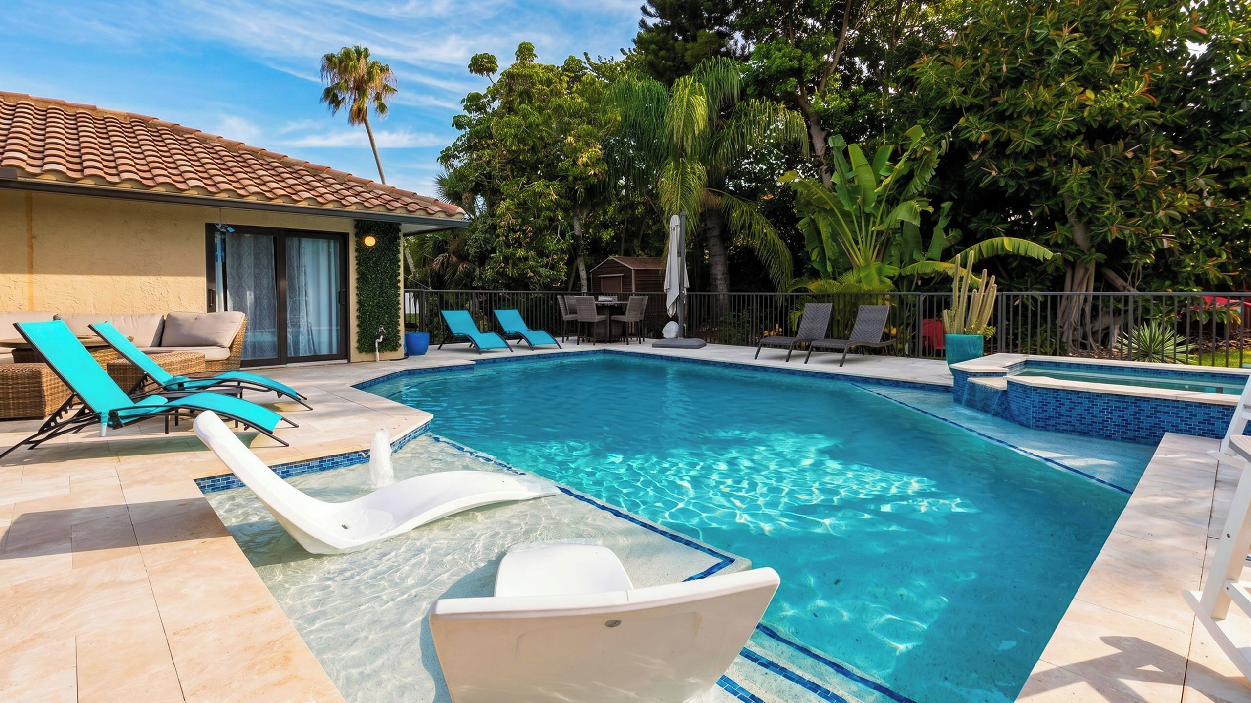 A swimming pool with clear blue water, surrounded by lounge chairs and a patio area.