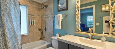 A bathroom with a bathtub, toilet, vanity with a large mirror, and a shower.