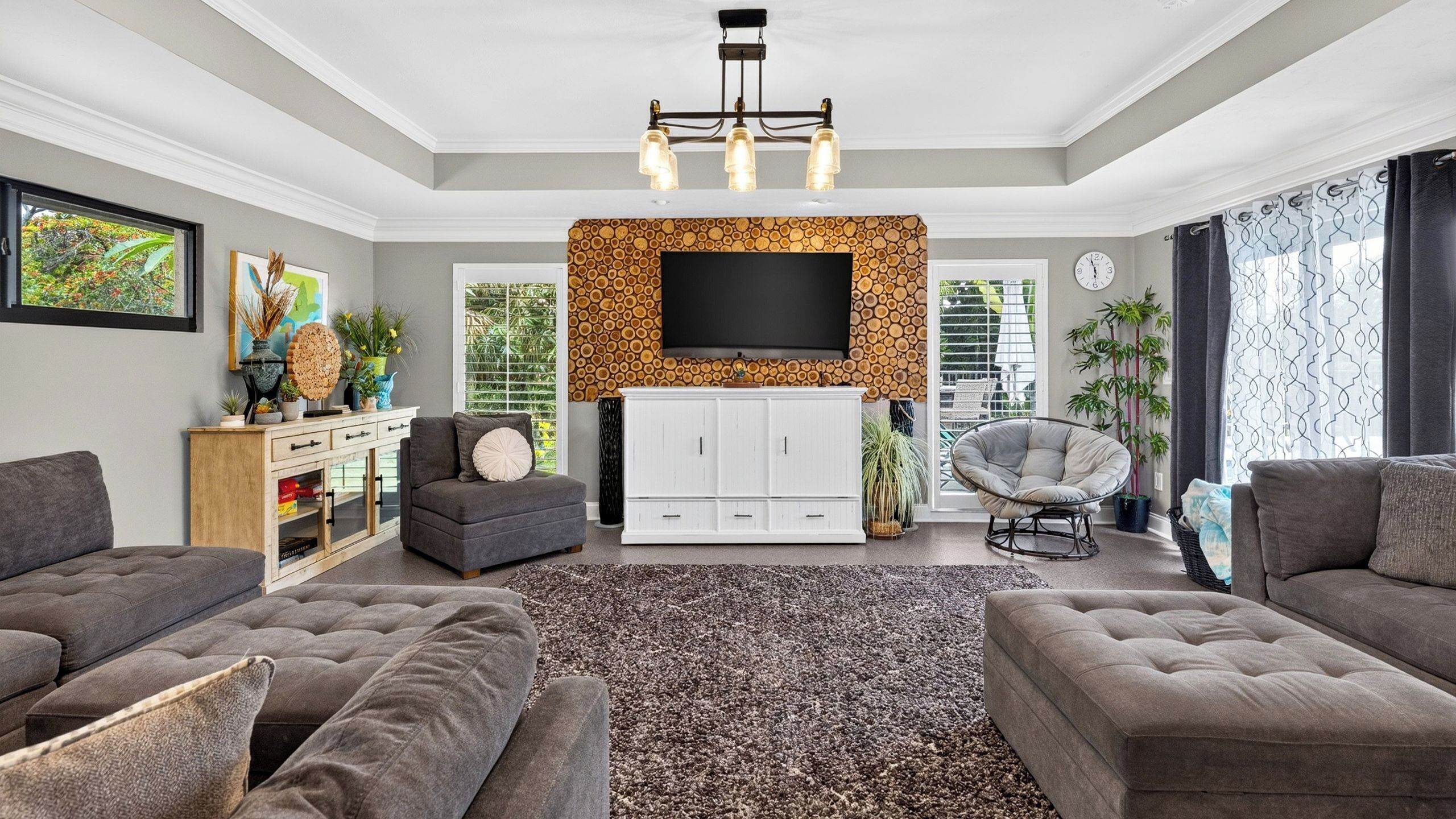 A living room with grey sofas, a white entertainment unit, a flat-screen TV, and a patterned wall.