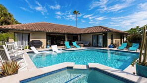 A pool with lounge chairs and a covered barbecue area. - Blue Sunset by Avantstay Pool + Spa + Fire Table Near Beaches + Naples (Bonita Springs)