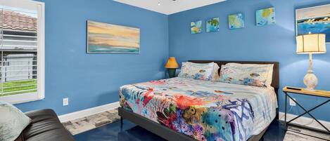 A bedroom with a bed, a ceiling fan, a window with blinds, and artwork on the walls.