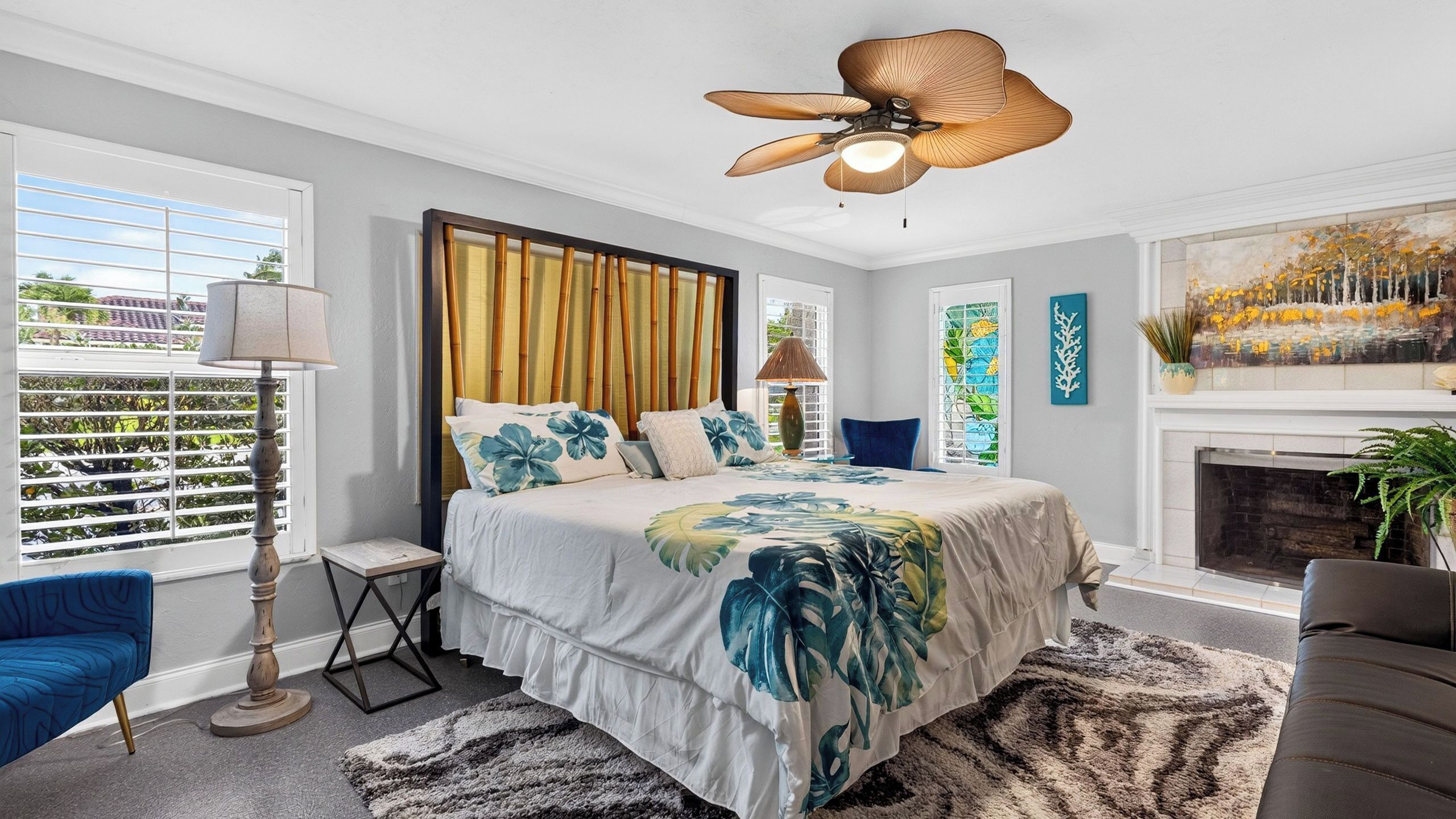 A bedroom with a bed, a ceiling fan, a window with blinds, a lamp, and a painting on the wall.