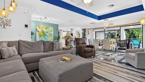 A modern living room with a sectional sofa, a coffee table, and a dining area with chairs and a table. - Blue Sunset by Avantstay Pool + Spa + Fire Table Near Beaches + Naples (Bonita Springs)