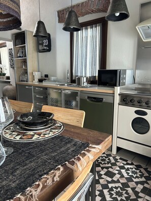 Eine moderne Küche mit Mikrowelle, Toaster und Backofen. Ein Holztisch mit schwarzem Platzsetzer und einem Glas.