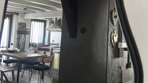 Reflexo num espelho de um quarto com mesa de jantar, cadeiras, cozinha e uma parede decorativa com um ornamento em forma de coração.