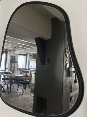 Spiegelbild eines Zimmers mit Esstisch, Stühlen, einer Küchenzeile und einer Wanddeko mit herzförmigem Ornament.