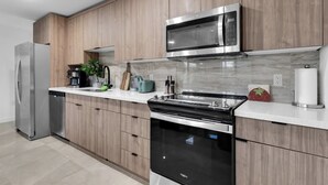 A modern kitchen with wooden cabinets, stainless steel appliances, and a marble backsplash. - El Mirador (Homestead)