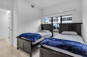 Ein Zimmer mit zwei Betten, einer Tür und einem Fenster mit Blick auf Gebäude.