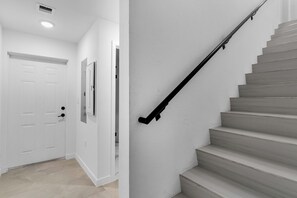 Eine Treppe mit schwarzer Handlauf, einer weißen Tür und einem hellen Boden.