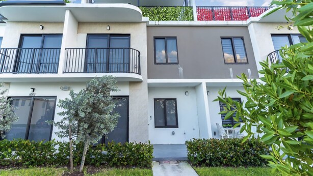A modern multi-story residential building with balconies, a flat roof, and a small garden area. - El Mirador (Homestead)