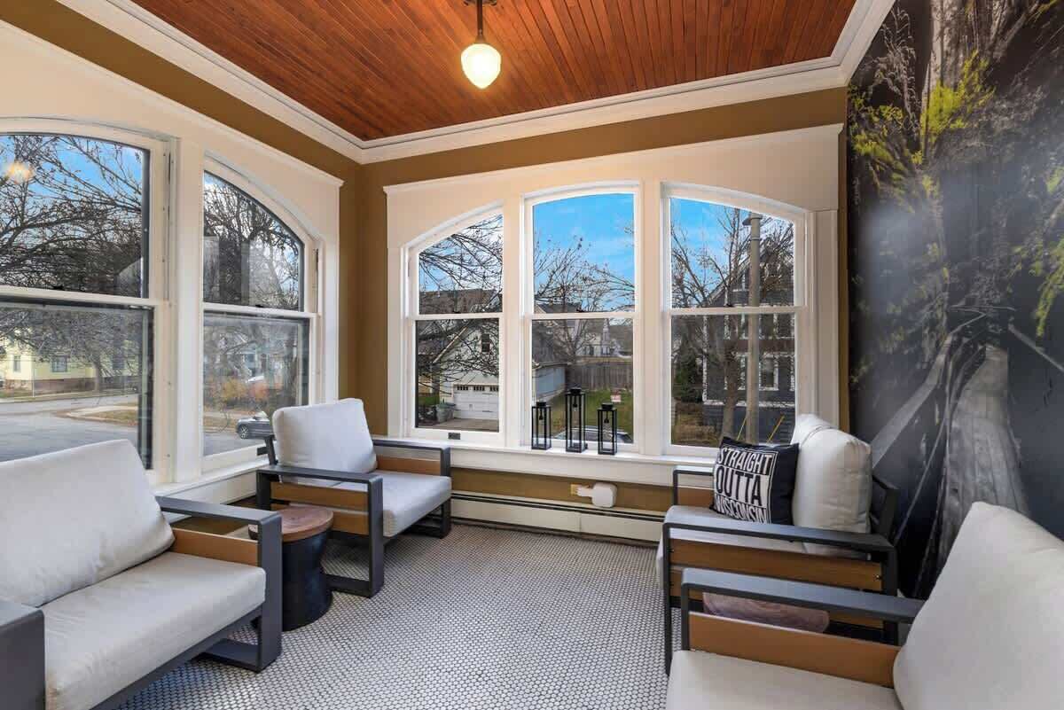 A sunroom with large windows, a wooden ceiling, and a seating area with sofas and tables.
