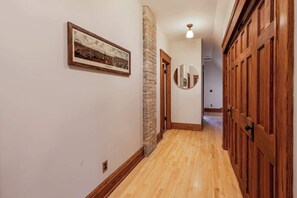 A hallway with wooden flooring, a stone pillar, a framed picture on the wall, and wooden doors. - 5BR Luxury Retreat With Huge Garage & 3 King Beds! (Milwaukee)