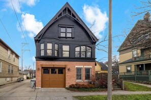 A two-story house with a brown garage door, a brick facade, and a large window on the upper floor. - 5BR Luxury Retreat With Huge Garage & 3 King Beds! (Milwaukee)