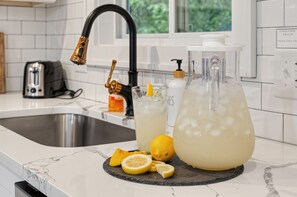 A kitchen with a stainless steel sink, a black faucet, a glass pitcher, and a glass with a lemon slice.