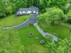 A house with a paved driveway, a lawn, and a small pond with seating. - Luxe Highlands Hot Tub Retreat w Fire Pit! (Highlands)