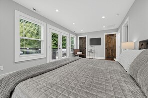 A bedroom with a large bed, a flat-screen TV, and a view of the outdoors through the windows.