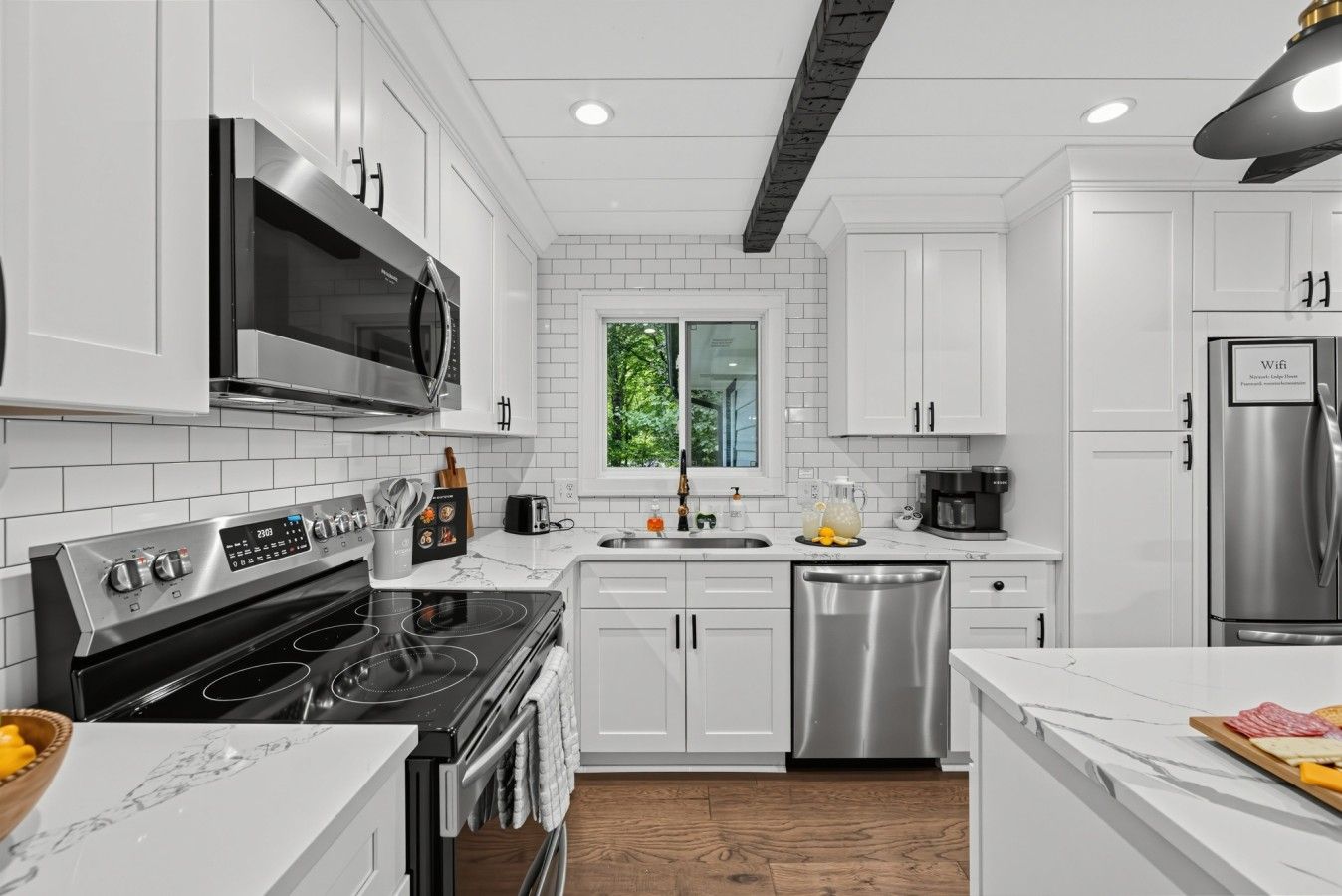 A modern kitchen with white cabinetry, stainless steel appliances, and a wooden floor.