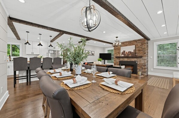 A modern dining area with a wooden table set for six, surrounded by grey upholstered chairs.