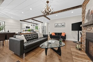 A modern living room with a leather sofa, a glass coffee table, and a fireplace. - Luxe Highlands Hot Tub Retreat w Fire Pit! (Highlands)