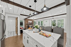 A modern kitchen with a marble island, pendant lighting, and a brick accent wall. - Luxe Highlands Hot Tub Retreat w Fire Pit! (Highlands)