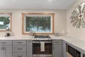 A modern kitchen with a built-in oven, a window with a view of trees, and a decorative wall clock. - Private 60-Acre Mountain Retreat | Hot Tub & Views (Pine)