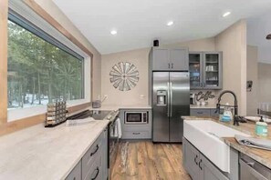 A modern kitchen with a microwave, refrigerator, and a large window. - Private 60-Acre Mountain Retreat | Hot Tub & Views (Pine)