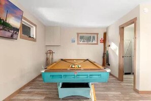 A pool table in a room with a wooden floor, a window, and framed pictures on the wall. - Private 60-Acre Mountain Retreat | Hot Tub & Views (Pine)