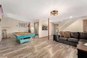 Ein Zimmer mit Billardtisch, einer Couch und einer Treppe.