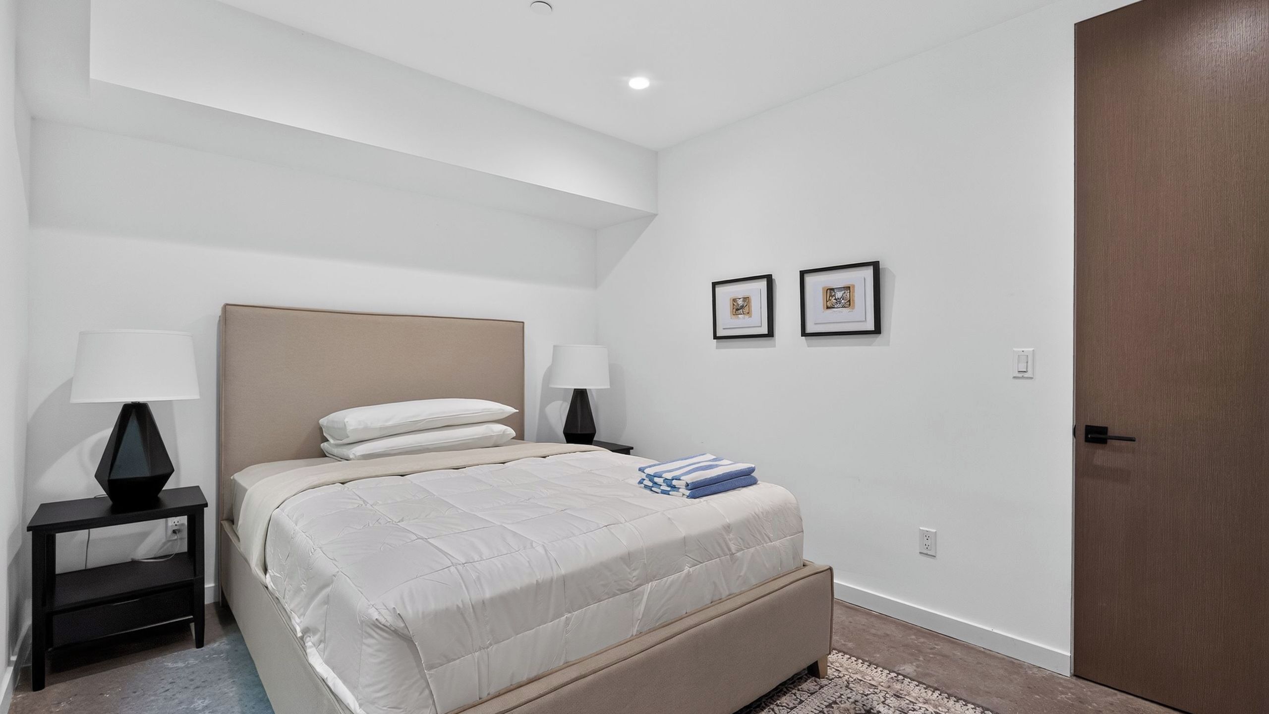 Ein Schlafzimmer mit einem Bett, zwei Nachttischen, einer Kommode, einer Tür und zwei gerahmten Bildern an der Wand.