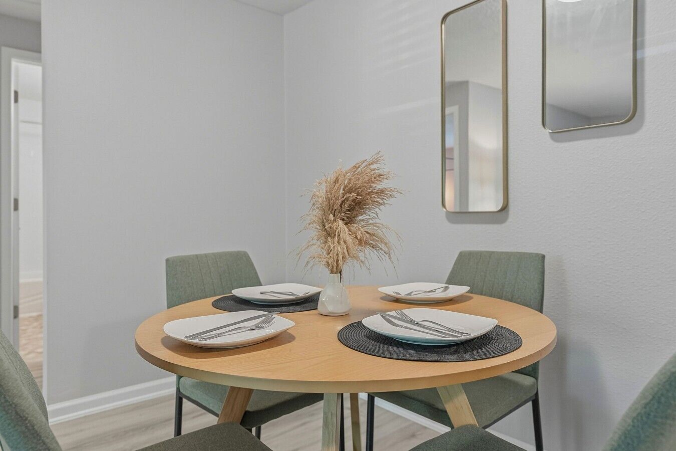 Een eethoek met een ronde tafel, vier stoelen en een vaas met gedroogde planten.
