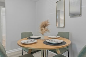 Uma área de refeições com uma mesa redonda, quatro cadeiras e um vaso com plantas secas.
