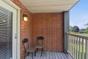 A covered porch with a brick wall, two chairs, a door with blinds, and a view of a grassy area. - King Canopy Bed I Sofa Bed I Next to Restaurants (Kettering)