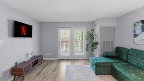 A modern living room with a flat-screen TV, a green sofa, a wooden entertainment unit, and a door with glass panels. - King Canopy Bed I Sofa Bed I Next to Restaurants (Kettering)