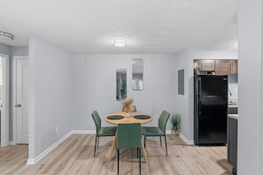 A modern kitchen with a black refrigerator, a dining area with a round table and green chairs, and a light-colored wooden floor. - King Canopy Bed I Sofa Bed I Next to Restaurants (Kettering)