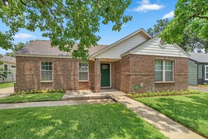 A single-story brick house with a green door, a small front porch, and a well-maintained lawn. - Near UH, Rice University, Texas Medical Center & Downtown w/ Game Room (Houston)