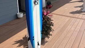 Una tabla de surf apoyada contra un edificio, con una planta en maceta a su lado.
