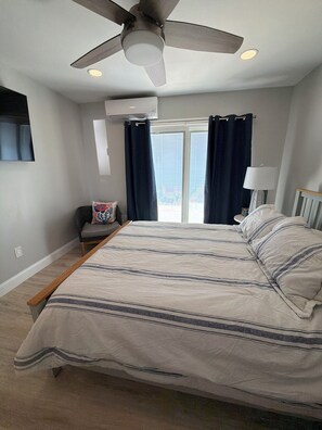 A bedroom with a bed, a ceiling fan, a window with curtains, a chair, and a lamp. - Cozy 1-bedroom condo in amazing Cape May with AC (Cape May)