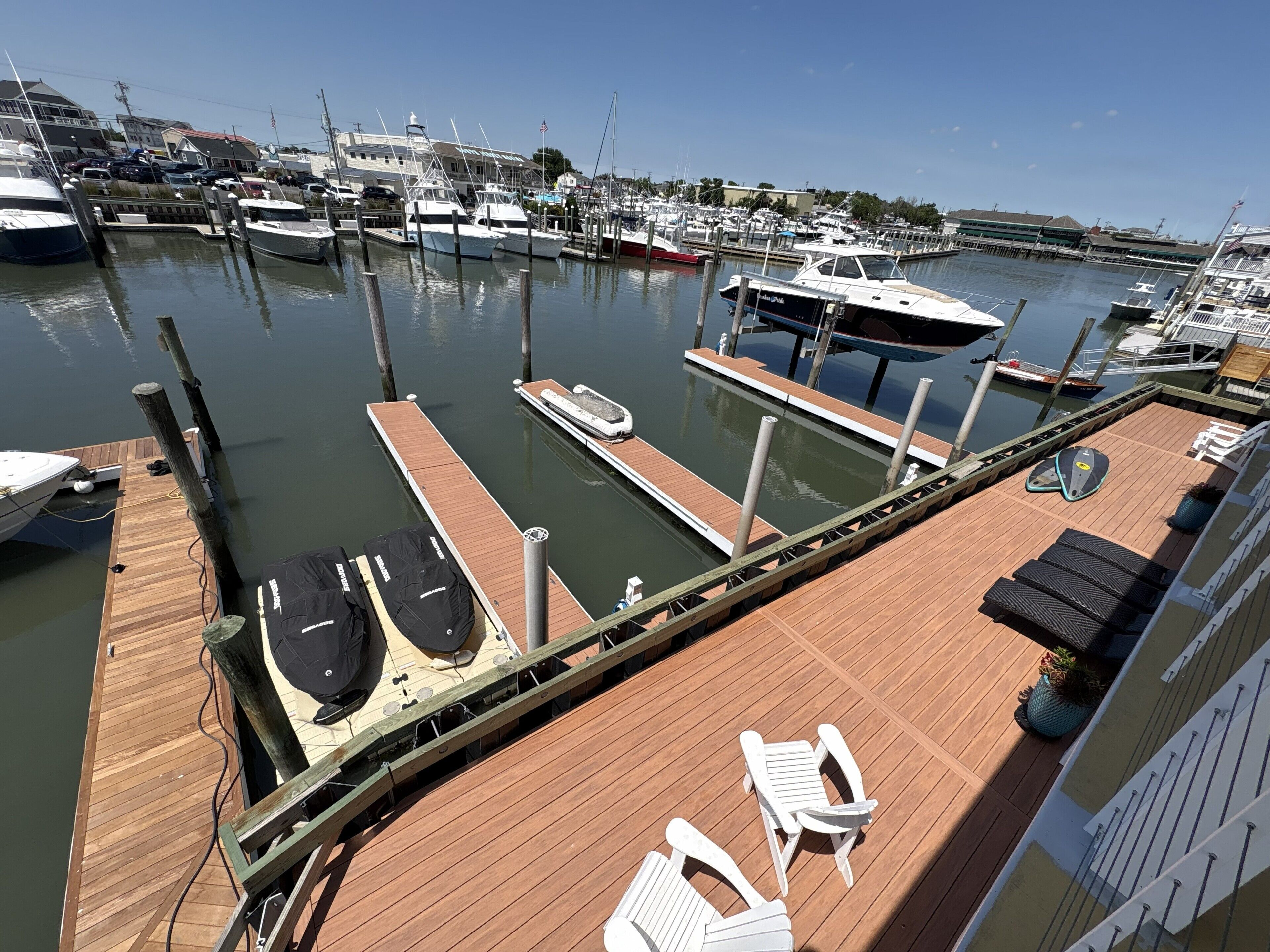 Un puerto deportivo con varias embarcaciones amarradas, una terraza de madera con sillones de descanso, y vista al puerto en el fondo.