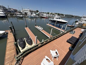 A marina with multiple boats docked, a wooden deck with lounge chairs, and a view of the marina in the background. - Cozy 1-bedroom condo in amazing Cape May with AC (Cape May)