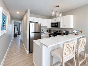 A modern kitchen with white cabinetry, stainless steel appliances, and a central island with bar stools. - Cape May Harbor Getaway with Kayaks & Bikes (Cape May)